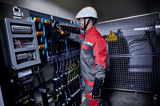 Ein Energieversorger trägt Multinorm Schutzkleidung und arbeitet in einem Raum mit Stromschalter.